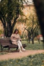 A Caucasian girl in a beige coat and blue jeans sits on a bench in a park in autumn and reads a book Royalty Free Stock Photo