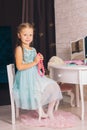 caucasian girl in a blue dress sits on a chair at the dressing table and holds pink beads in her hands Royalty Free Stock Photo