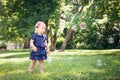 Caucasian girl child in blue dress standing in field meadow park outside, making soap bubbles Royalty Free Stock Photo