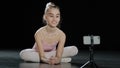 Caucasian girl child teen ballerina gymnast sitting on floor in dance hall waving hello to mobile phone camera online Royalty Free Stock Photo