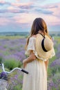 Caucasian girl in a light dress and hat with a bicycle in a lavender field, view from the back. Royalty Free Stock Photo