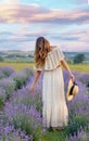 Caucasian girl in a light dress and hat walking in a lavender field, view from the back. Royalty Free Stock Photo