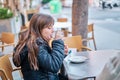 Caucasian girl with long hair and in a coat sitting on a terrace of a bar having a cocoa drink Royalty Free Stock Photo