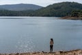 Caucasian girl looking at the lake water of Apartadura dam with mountains with trees landscape in Alentejo, Portugal