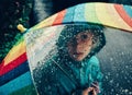 Caucasian girl looking through rainbow umbrella with large rain drops