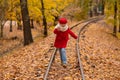 Caucasian girl in a red coat and beret walks along the railway tracks in the park in autumn. Royalty Free Stock Photo