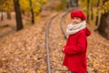 Caucasian girl in a red coat and beret walks along the railway tracks in the park in autumn. Royalty Free Stock Photo