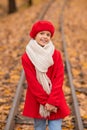 Caucasian girl in a red coat and beret walks along the railway tracks in the park in autumn. Royalty Free Stock Photo