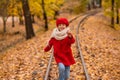 Caucasian girl in a red coat and beret walks along the railway tracks in the park in autumn. Royalty Free Stock Photo