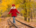 Caucasian girl in a red coat and beret walks along the railway tracks in the park in autumn. Royalty Free Stock Photo