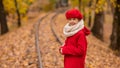 Caucasian girl in a red coat and beret walks along the railway tracks in the park in autumn. Royalty Free Stock Photo