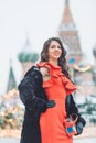 Caucasian girl in a red dress holds in hand an accordion in the winter during a blizzard against the background of St. Basil`s C Royalty Free Stock Photo