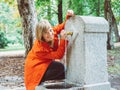 Caucasian girl with red gabardine drinks water from a fountain in a park in Madrid