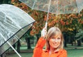 Caucasian girl in red gabardine plays with two transparent umbrellas in a park