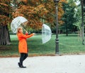 Caucasian girl in red gabardine plays with two transparent umbrellas in a park