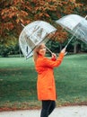 Caucasian girl in red gabardine plays with two transparent umbrellas in a park