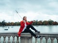 Caucasian girl with red gabardine and transparent umbrella sitting next to the Retiro Park lake in Madrid, Spain