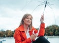 Caucasian girl with red gabardine and transparent umbrella sitting next to the Retiro Park lake in Madrid, Spain