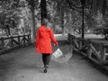 A Caucasian girl with a red gabardine walks through a park with a transparent umbrella in her hand