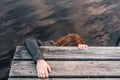 caucasian girl with reddish hair holding on to the wooden slats of the jetty trying to climb up from the lake water