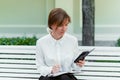 Caucasian girl sits on a park bench and looks into the phone and writes in a notebook Royalty Free Stock Photo