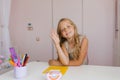 Caucasian girl is sitting at a desk with a notebook and stationery on it, raising her hand up at school Royalty Free Stock Photo