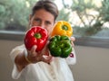 Caucasian girl sitting in her kitchen showing three big colored peppers. Green, red and yellow Royalty Free Stock Photo