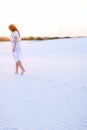 Caucasian girl wearing white dress walking barefoot on sand. Royalty Free Stock Photo