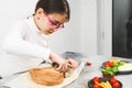 Caucasian girl in a white turtleneck cuts dough on a wooden plate with a metal scabbard. Royalty Free Stock Photo