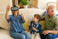 Caucasian grandfather and grandson watching grandmother wearing vr headset sitting on couch at home