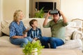 Caucasian grandmother and grandson watching grandfather wearing vr headset sitting on couch at home