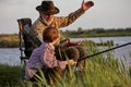 grey-headed grandfather having talk with grandson while fishing together on lake Royalty Free Stock Photo