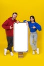 Caucasian guy and asian girl leaned on huge, giant smartphone standing on old books with white screen pointing at it Royalty Free Stock Photo