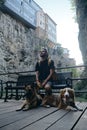 Caucasian guy with dreadlocks is sitting on bench in center of old town with two dogs and enjoying architecture Royalty Free Stock Photo