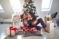 Caucasian guy hugging beautiful brunette in front of christmas tree beside pile of presents