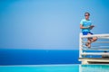 Caucasian guy relaxing near pool with amazing view and reading book in Greece. Beautiful famous background Royalty Free Stock Photo