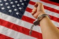 caucasian hand cuffed with silver metal handcuffs over US flag background