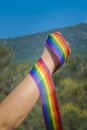 Caucasian hand fist holding rainbow ribbon at the outdoors with clear blue sky. Lgtbiq concept