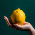 A Caucasian hand holding a single lemon with a dark green background