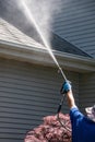 A caucasian hand with a latex glove arm holding a water sprayer wand power washing the gutters and roof of a house Royalty Free Stock Photo