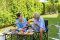 Caucasian handicapped elderly people with mobility walker camping with Asian woman caregivers at home garden to relax and