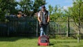 Caucasian handsome guy mowing grass with an electric lawn mower in garden with trees. Young man gardener mows the grass Royalty Free Stock Photo