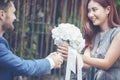 Caucasian handsome man giving flowers to asian girlfriend asking for proposing to marry him at green park. Couple lover on Royalty Free Stock Photo