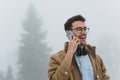 Caucasian handsome man smiling while having conversation on mobile phone with his friend, wearing trendy coat and eyeglasses in Royalty Free Stock Photo