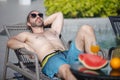 Caucasian handsome man wearing sunglasses lying at near swimming pool, weekend relax luxury travel poolside. Summer vacation Royalty Free Stock Photo