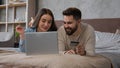 Caucasian happy couple woman and man relax on bed with laptop shopping online use bank credit card pay order buying in Royalty Free Stock Photo