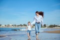 Caucasian happy young mother and daughter smiling while running on the beach, leaving footsteps on the wet sand Royalty Free Stock Photo