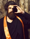 Caucasian hipster in suit holding perfume on brown vintage wooden studio background