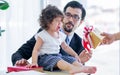 Caucasian little girl is crying hard with sadness while sitting on table near window at home with blur background of her father. Royalty Free Stock Photo