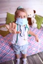 Caucasian little girl in a medical mask at home in her room. Quarantine protection against coronavirus. Home insulat Royalty Free Stock Photo